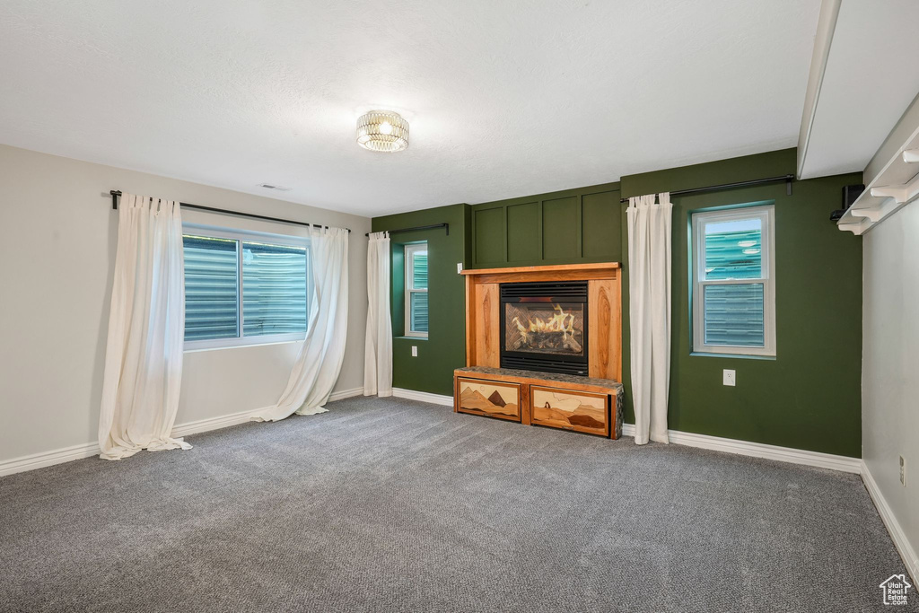 Unfurnished living room featuring carpet flooring and a glass covered fireplace