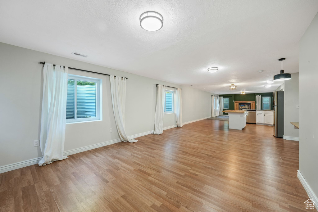 Unfurnished living room with light wood-type flooring, plenty of natural light, and a lit fireplace