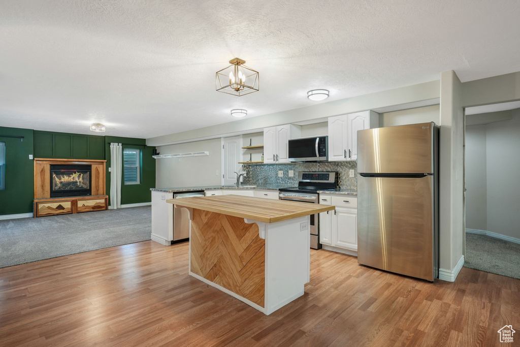 Kitchen with stainless steel appliances, butcher block countertops, white cabinetry, and decorative backsplash