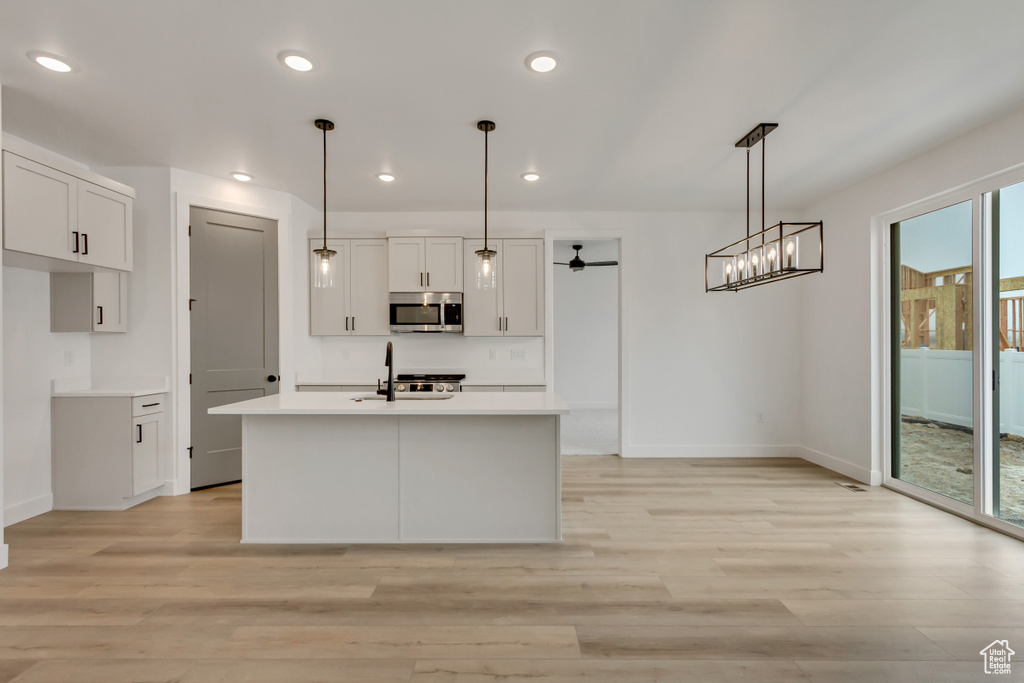 Kitchen with stainless steel microwave, light wood-style flooring, white cabinetry, ceiling fan, and light countertops