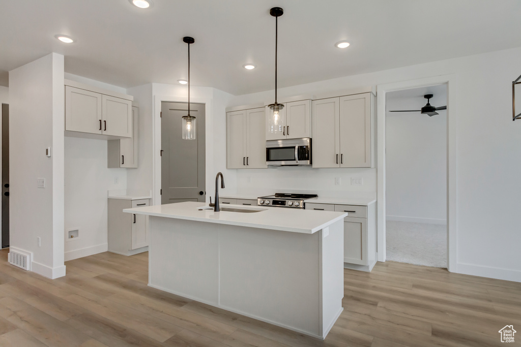 Kitchen with stainless steel appliances, a kitchen island with sink, light wood-style flooring, light countertops, and recessed lighting