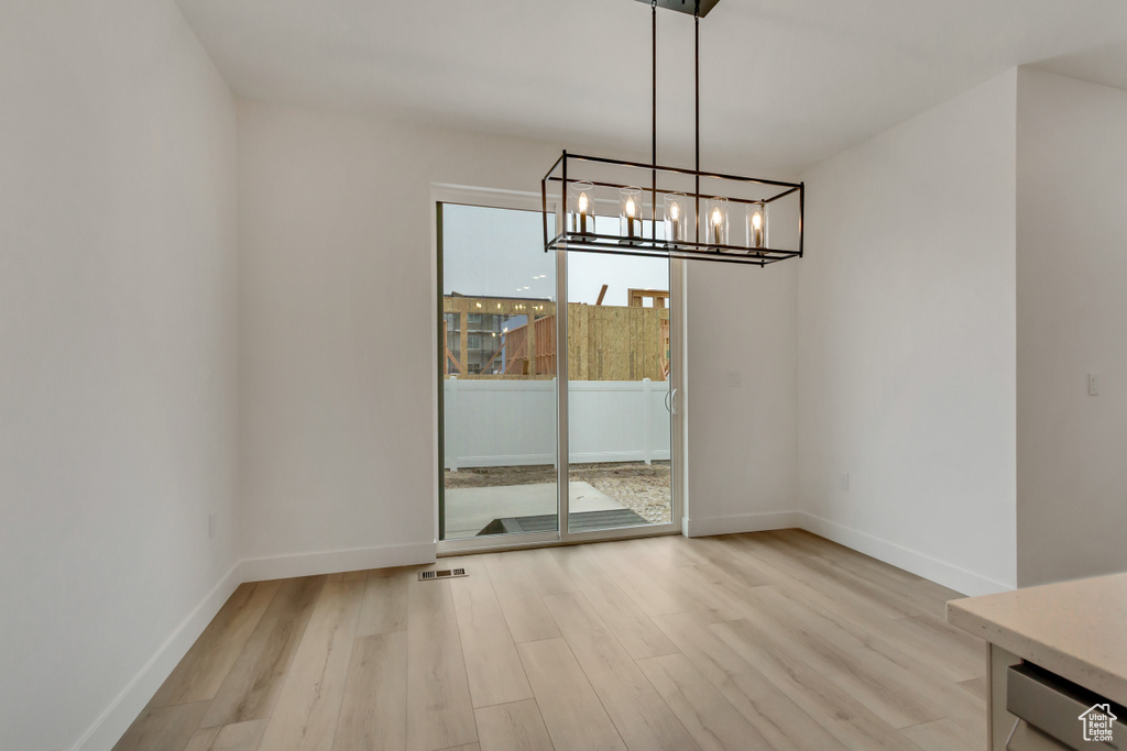 Unfurnished dining area featuring light wood-style flooring and a chandelier