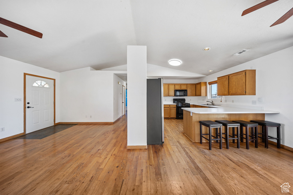 Kitchen featuring a ceiling fan, black appliances, vaulted ceiling, light wood-style floors, and light countertops