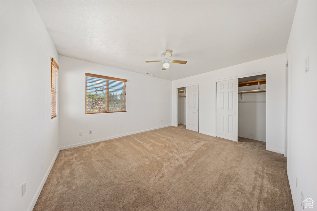 Unfurnished bedroom with two closets, light carpet, and ceiling fan