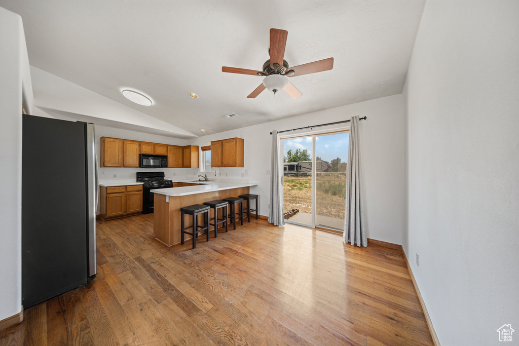 Kitchen with black appliances, a peninsula, brown cabinets, light wood-style floors, and light countertops