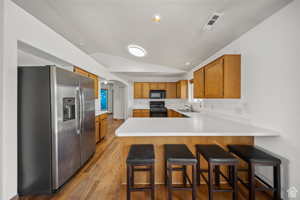 Kitchen with black appliances, lofted ceiling, a peninsula, arched walkways, and wood finished floors