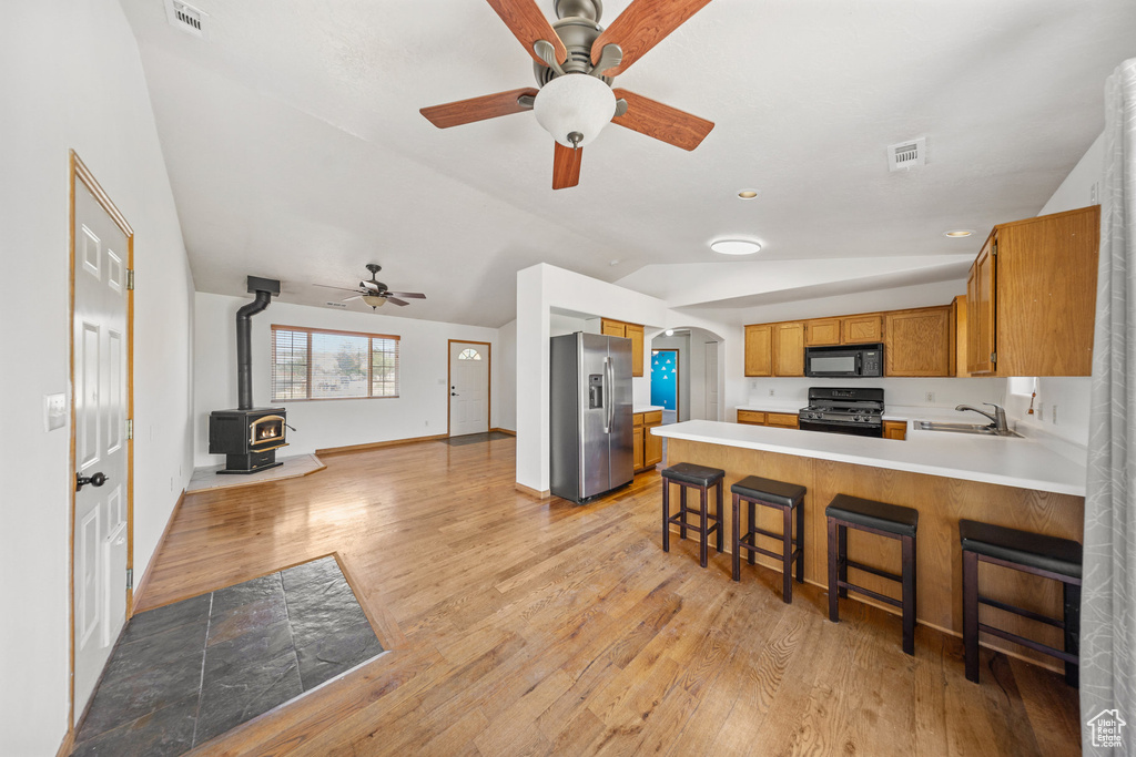 Kitchen with black appliances, vaulted ceiling, a wood stove, light countertops, and open floor plan