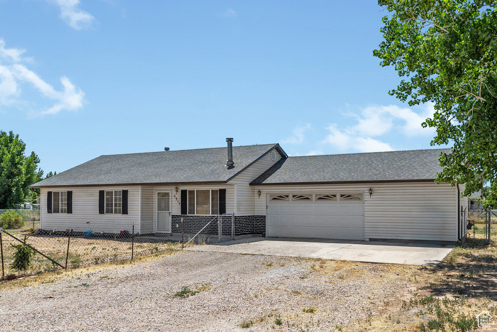 Ranch-style house featuring dirt driveway, an attached garage, and a shingled roof