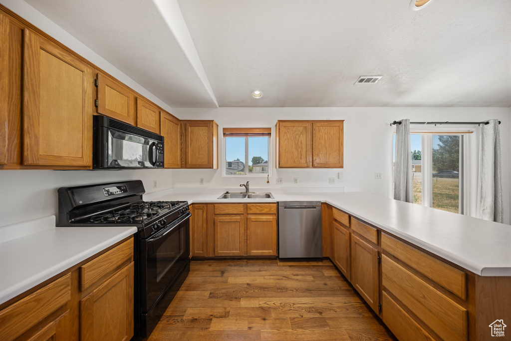 Kitchen with black appliances, a peninsula, healthy amount of natural light, dark wood-style flooring, and recessed lighting