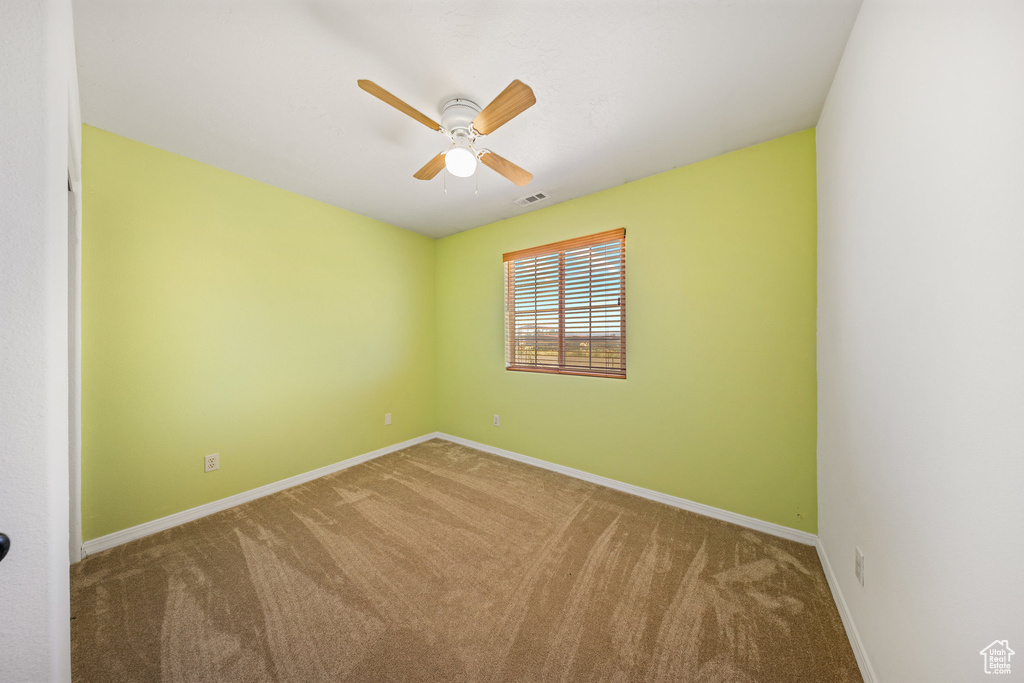 Carpeted spare room featuring a ceiling fan and baseboards