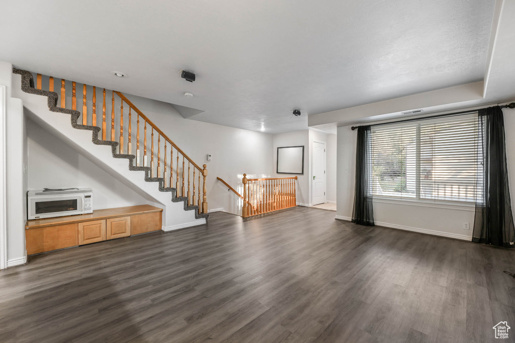 Unfurnished living room featuring dark wood finished floors and baseboards