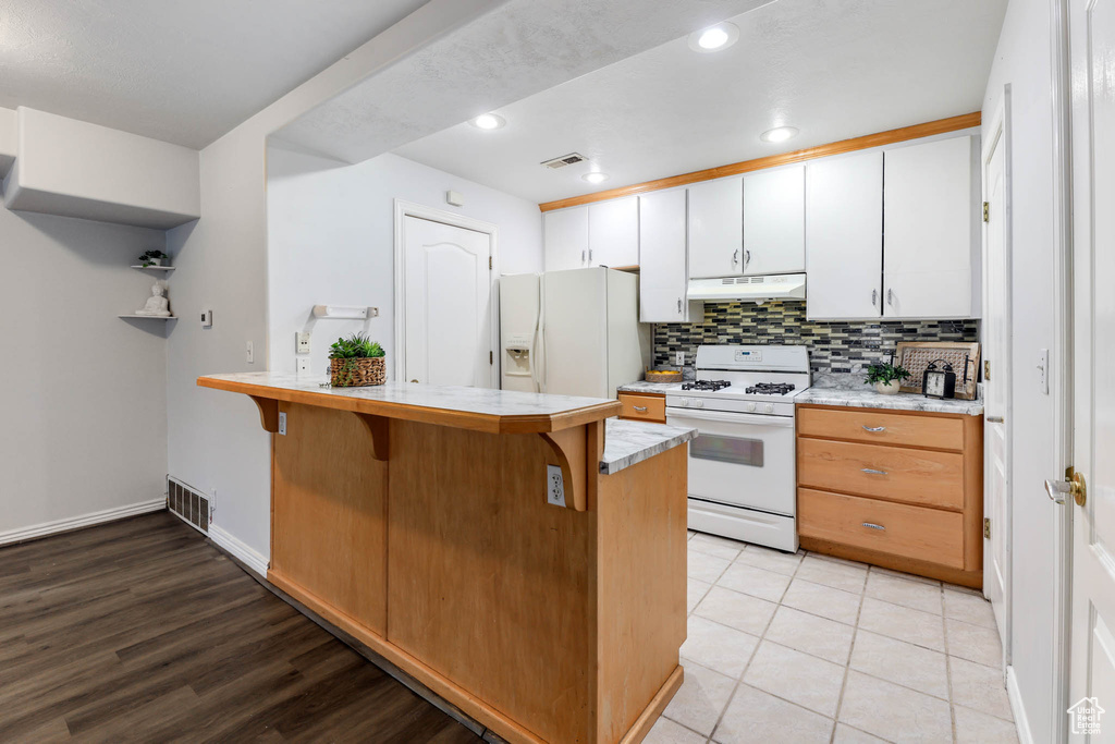 Kitchen featuring white appliances, under cabinet range hood, a peninsula, a kitchen breakfast bar, and light countertops