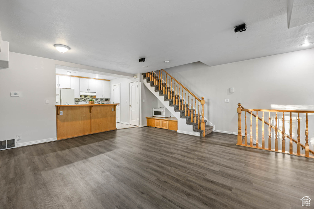 Unfurnished living room with dark wood-type flooring and stairway