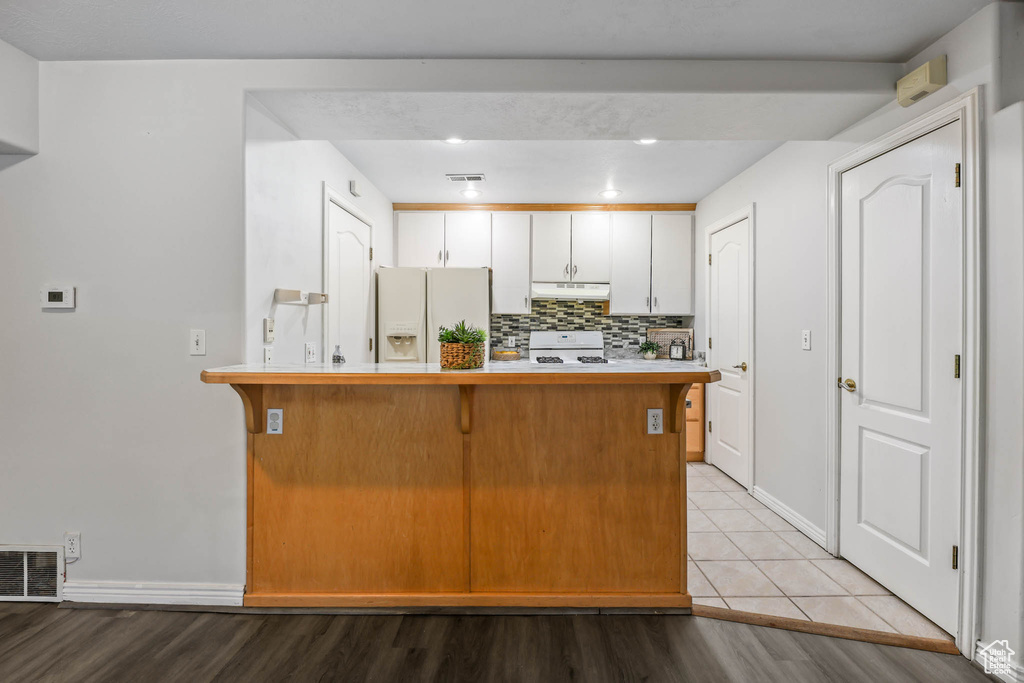 Kitchen featuring white refrigerator with ice dispenser, under cabinet range hood, stove, a kitchen bar, and a peninsula