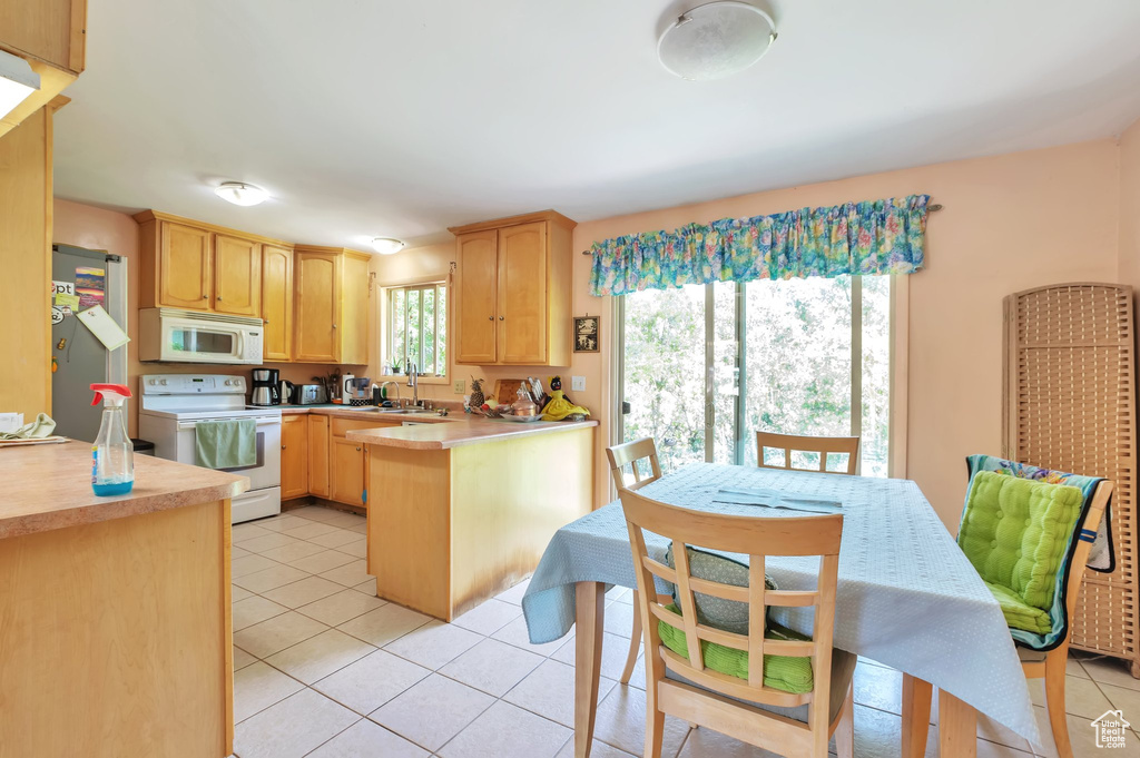 Kitchen with white appliances, light brown cabinetry, a peninsula, a heating unit, and light tile patterned floors