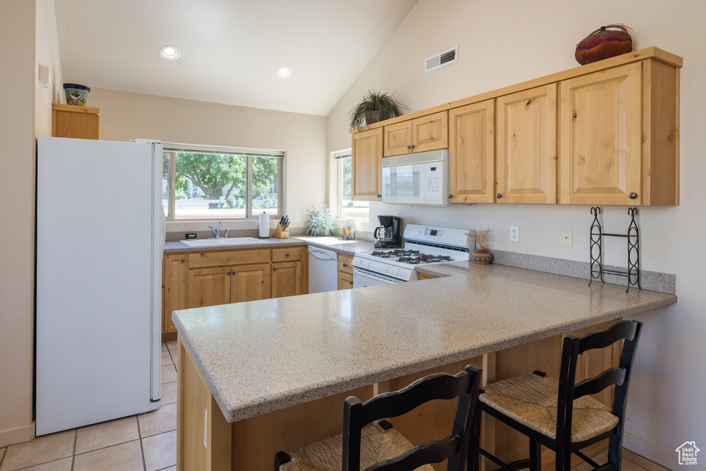 Kitchen featuring white appliances, light brown cabinetry, a peninsula, a kitchen breakfast bar, and recessed lighting