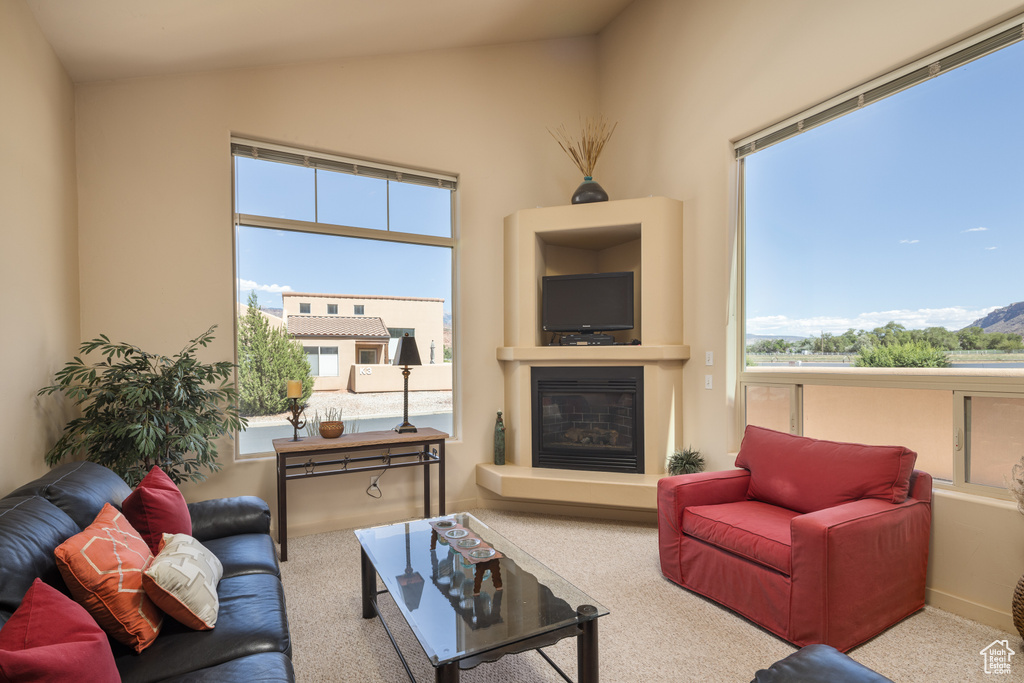Living area featuring carpet floors, lofted ceiling, a glass covered fireplace, and plenty of natural light