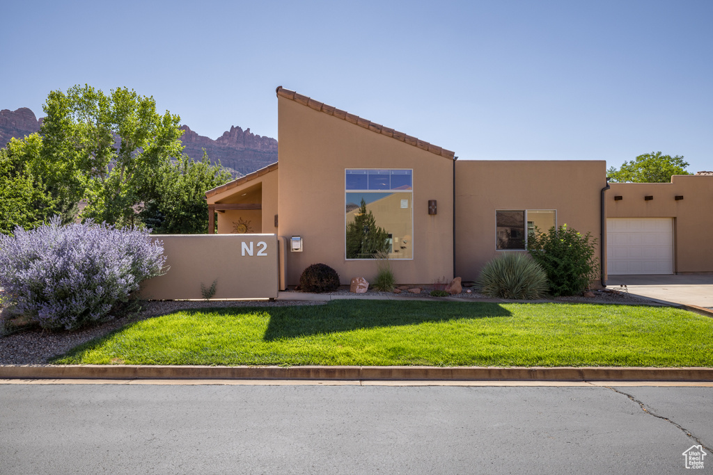 View of front of property featuring an attached garage, stucco siding, a mountain view, a front lawn, and driveway