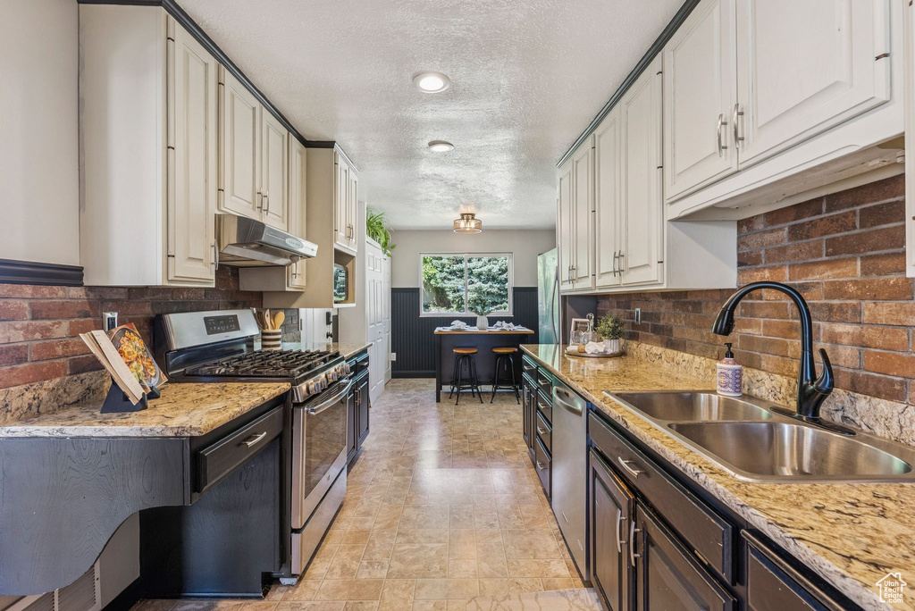 Kitchen featuring appliances with stainless steel finishes, under cabinet range hood, a textured ceiling, tasteful backsplash, and wainscoting