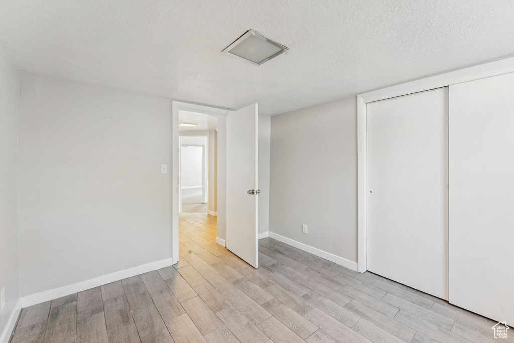 Unfurnished bedroom featuring light wood-style floors, a textured ceiling, and a closet