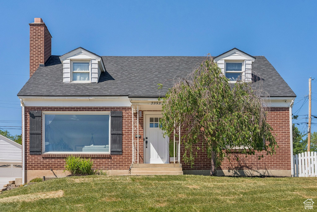 New england style home featuring brick siding, roof with shingles, and a chimney