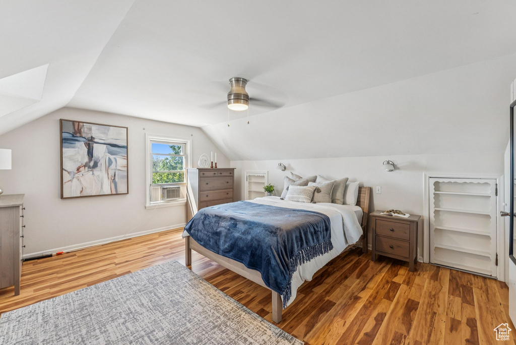 Bedroom with wood finished floors, lofted ceiling, ceiling fan, and cooling unit