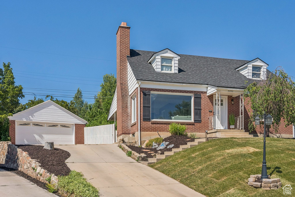 Cape cod home with brick siding, a chimney, an outbuilding, a detached garage, and a shingled roof