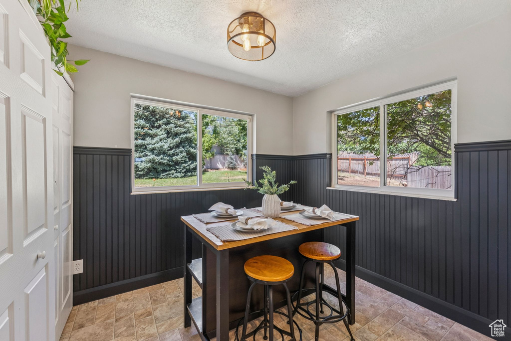Dining area featuring a wainscoted wall, a textured ceiling, light stone finish floors, healthy amount of natural light, and a chandelier