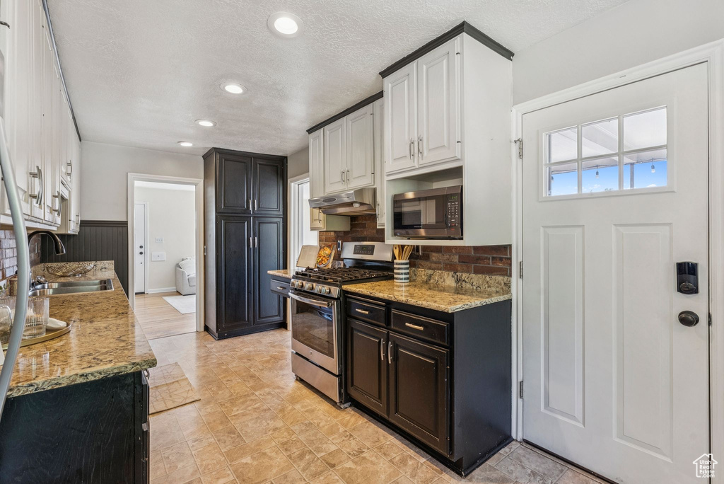 Kitchen with stainless steel appliances, under cabinet range hood, light stone countertops, decorative backsplash, and recessed lighting