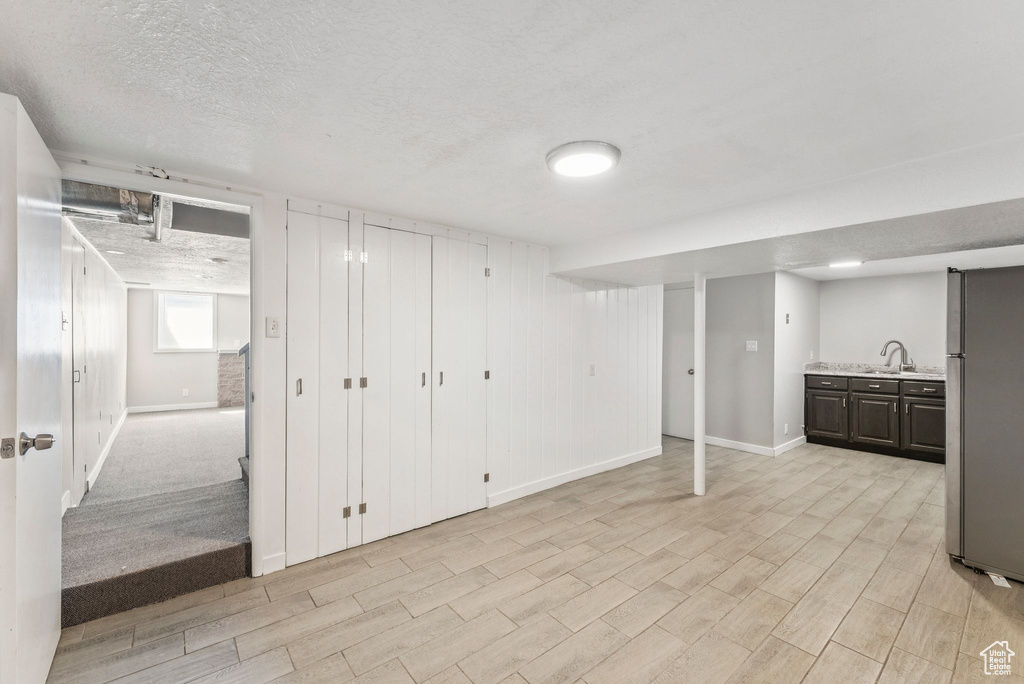 Basement with freestanding refrigerator, light wood-style flooring, and a textured ceiling