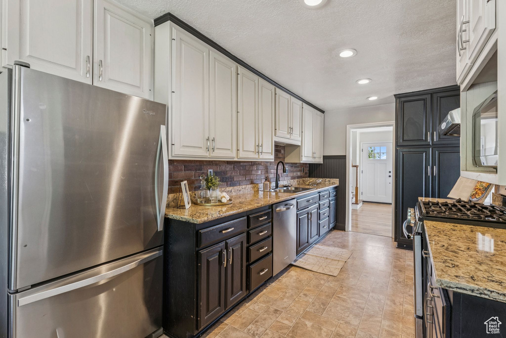 Kitchen featuring stainless steel appliances, white cabinetry, decorative backsplash, light stone counters, and recessed lighting