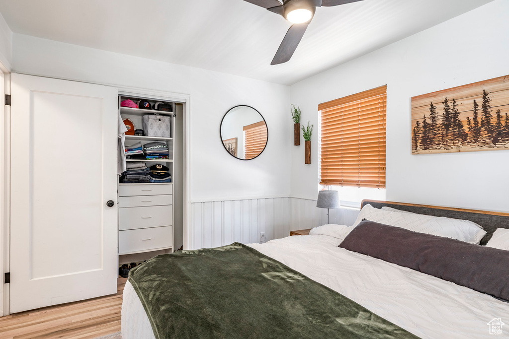 Bedroom featuring light wood-style flooring, a wainscoted wall, ceiling fan, and a closet