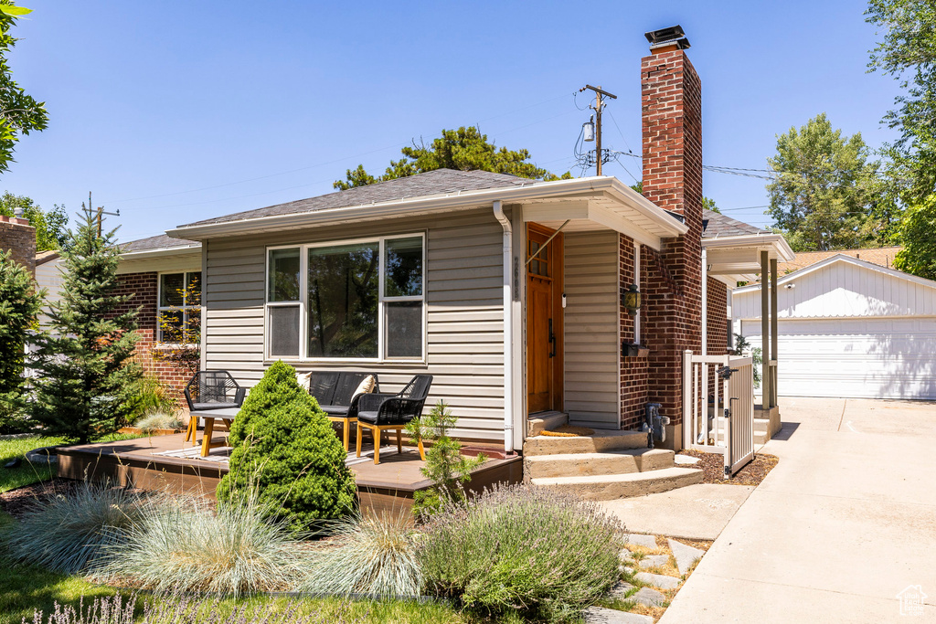 View of front of property featuring an outbuilding, a deck, a chimney, a garage, and a shingled roof