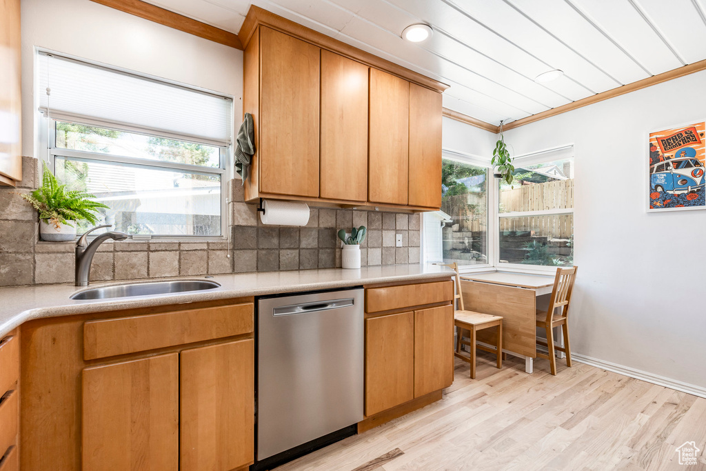 Kitchen featuring stainless steel dishwasher, ornamental molding, backsplash, light wood-style flooring, and light countertops