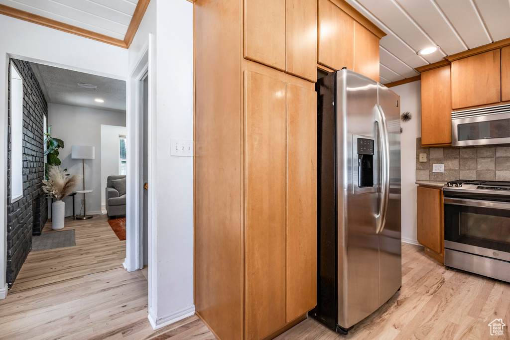 Kitchen featuring stainless steel appliances, light wood finished floors, backsplash, ornamental molding, and recessed lighting