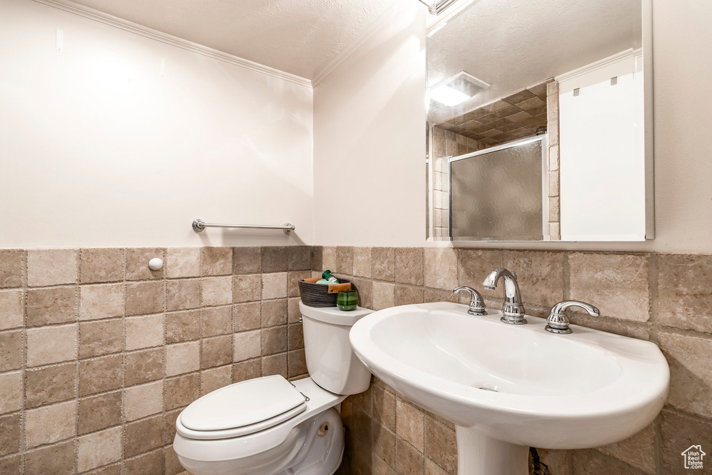 Bathroom with tile walls, a shower stall, crown molding, and wainscoting