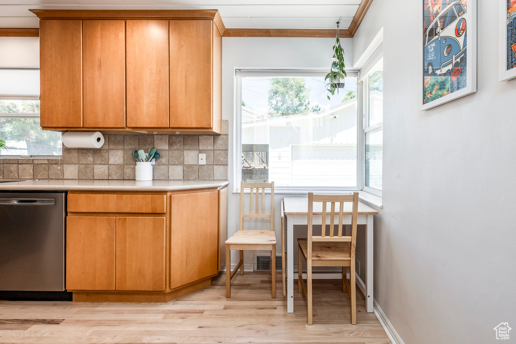 Kitchen with stainless steel dishwasher, light countertops, light wood finished floors, tasteful backsplash, and ornamental molding