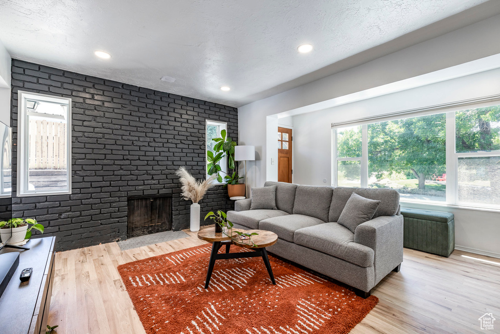 Living area with wood finished floors, a fireplace, brick wall, and recessed lighting
