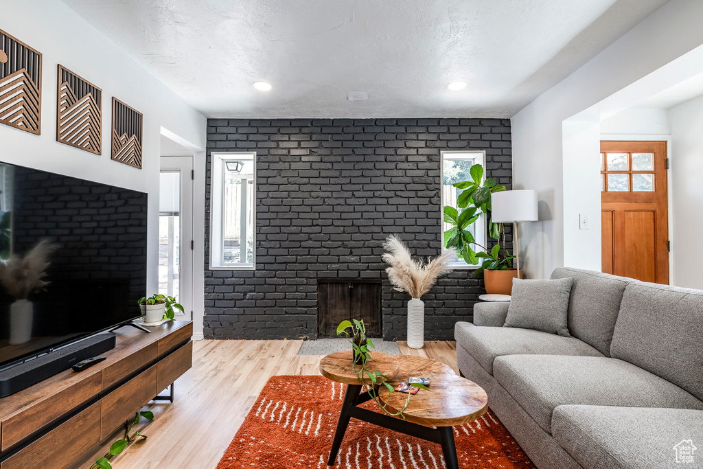 Living room featuring wood finished floors, a brick fireplace, recessed lighting, and brick wall