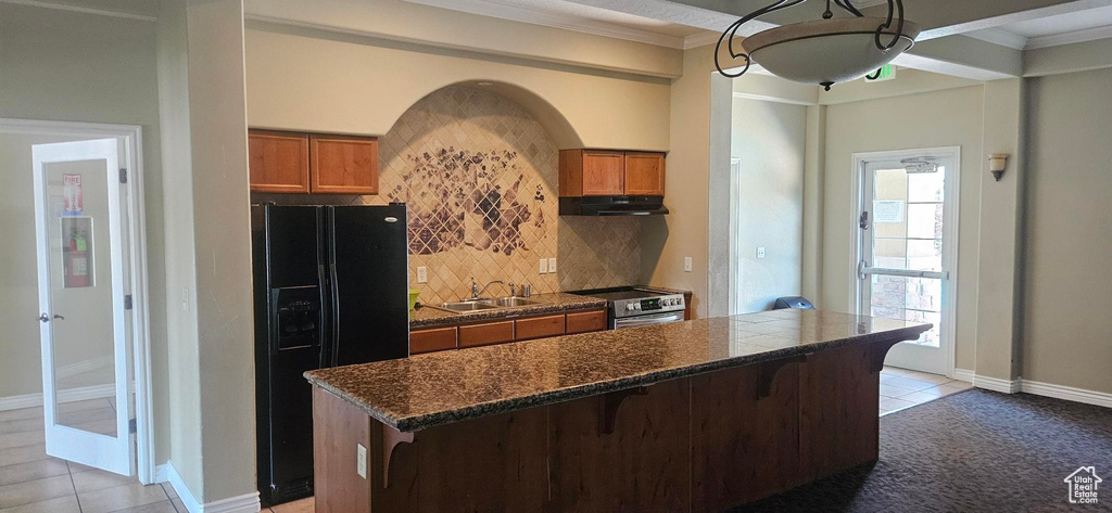 Kitchen featuring stainless steel electric stove, black fridge, dark countertops, brown cabinets, and crown molding