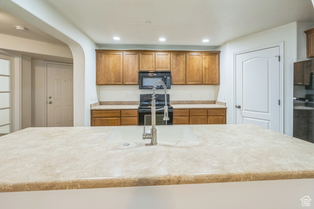 Kitchen with black appliances, brown cabinets, recessed lighting, arched walkways, and light stone counters