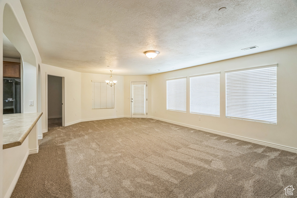 Unfurnished living room with a chandelier, a textured ceiling, and carpet flooring