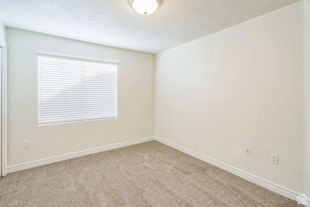 Carpeted empty room featuring a textured ceiling and baseboards
