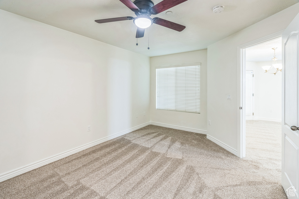 Empty room featuring a smoke detector, carpet flooring, a chandelier, and a ceiling fan