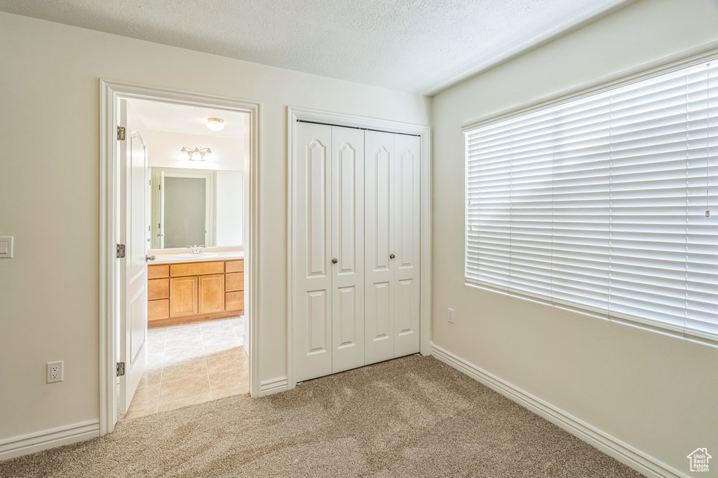 Unfurnished bedroom featuring light colored carpet, a textured ceiling, and a closet
