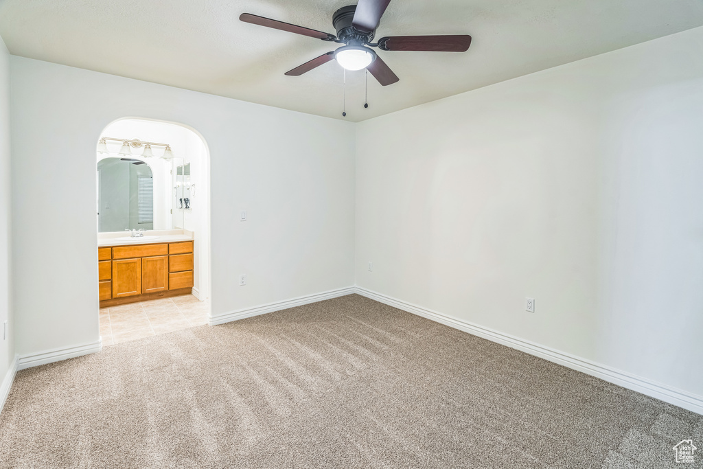 Unfurnished bedroom with light colored carpet, ensuite bath, arched walkways, and a ceiling fan