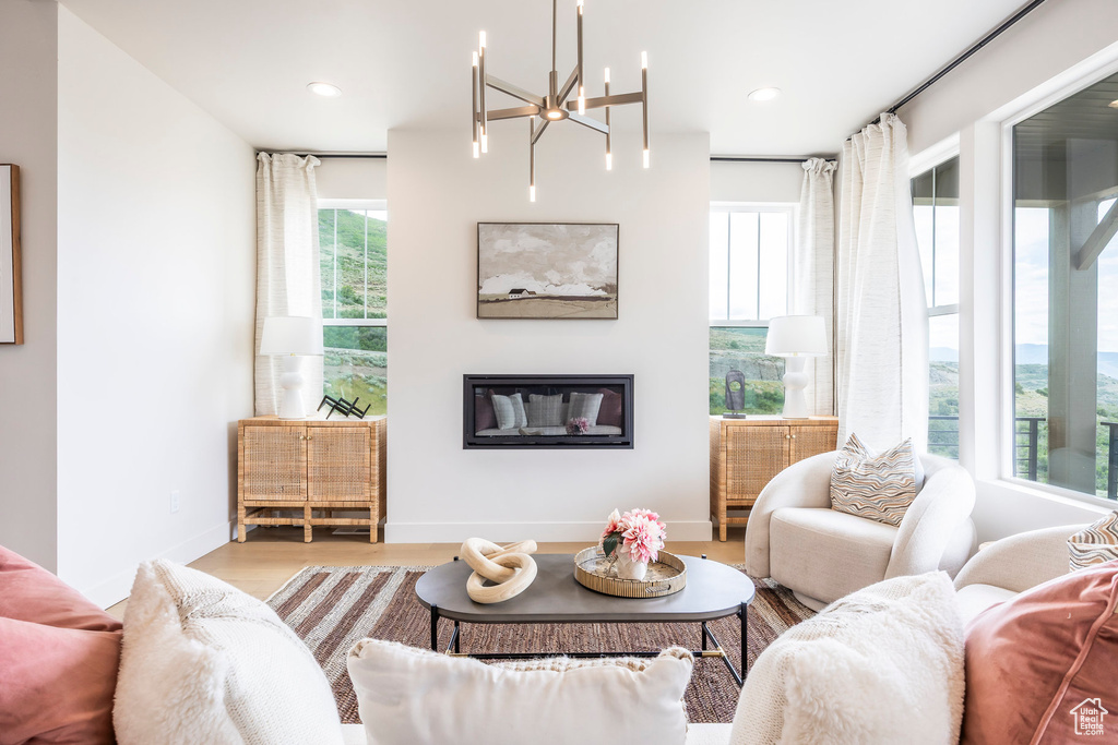 Living area with wood finished floors, a chandelier, a glass covered fireplace, and recessed lighting