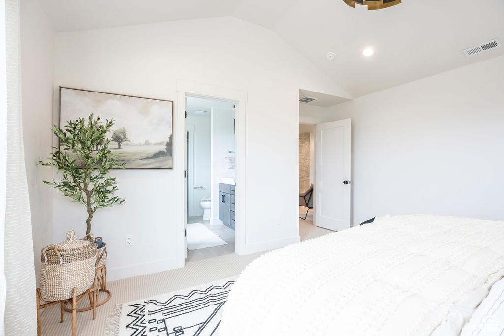 Bedroom with lofted ceiling, light carpet, and connected bathroom