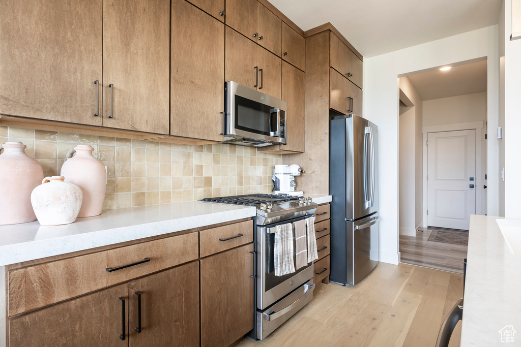 Kitchen featuring appliances with stainless steel finishes, light wood-type flooring, light countertops, and tasteful backsplash