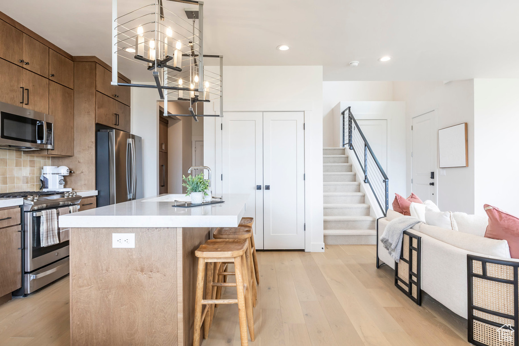 Kitchen with stainless steel appliances, a chandelier, brown cabinetry, light wood-type flooring, and recessed lighting